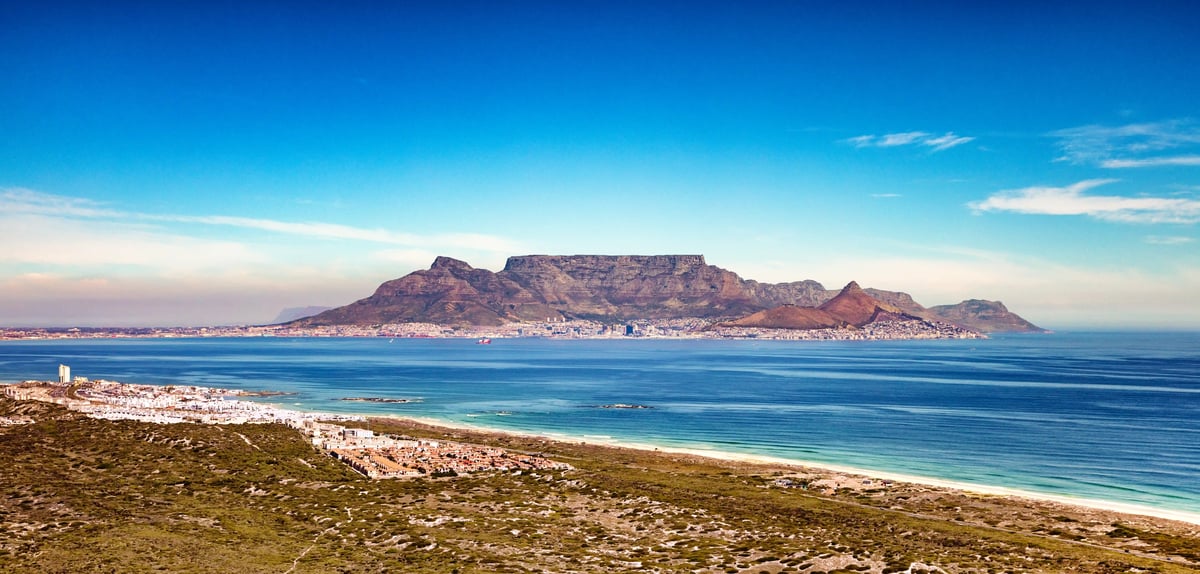 Blick über das Meer auf Kapstadt mit dem Tafelberg im Hintergrund und einer hellen Küstenlinie im Vordergrund