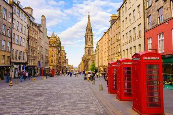 Historische Strasse in Edinburgh mit Kirchturm, alten Steinhäusern und roten Telefonzellen im Vordergrund