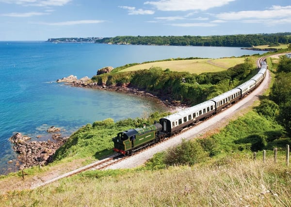 Historische Dampfeisenbahn fährt entlang einer grünen Küstenlandschaft mit Blick auf das blaue Meer