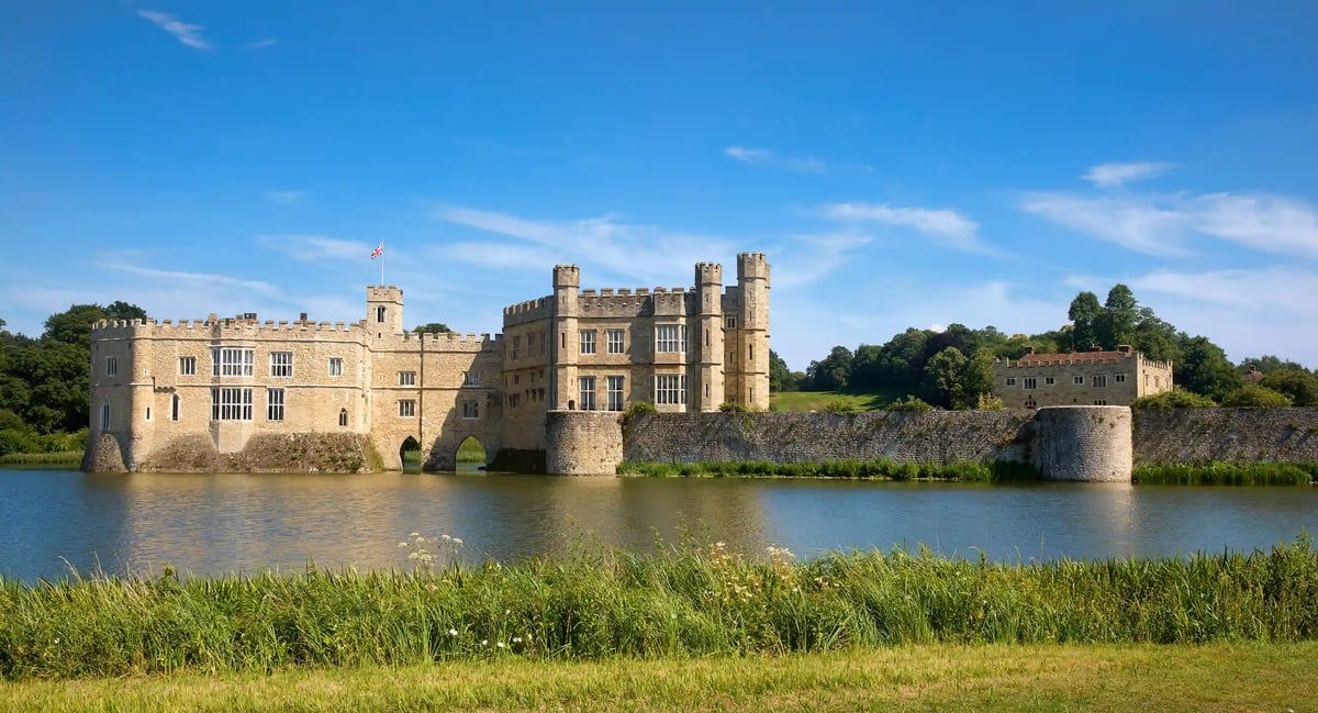 Leeds Castle mit Wassergraben und Türmen, gespiegelt in ruhigem Wasser vor blauem Himmel
