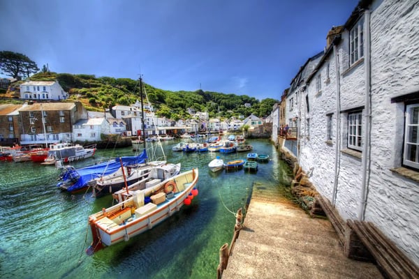 Kleiner Hafen in Polperro mit bunten Booten im klaren Wasser, weissen Häusern und grünen Hügeln im Hintergrund