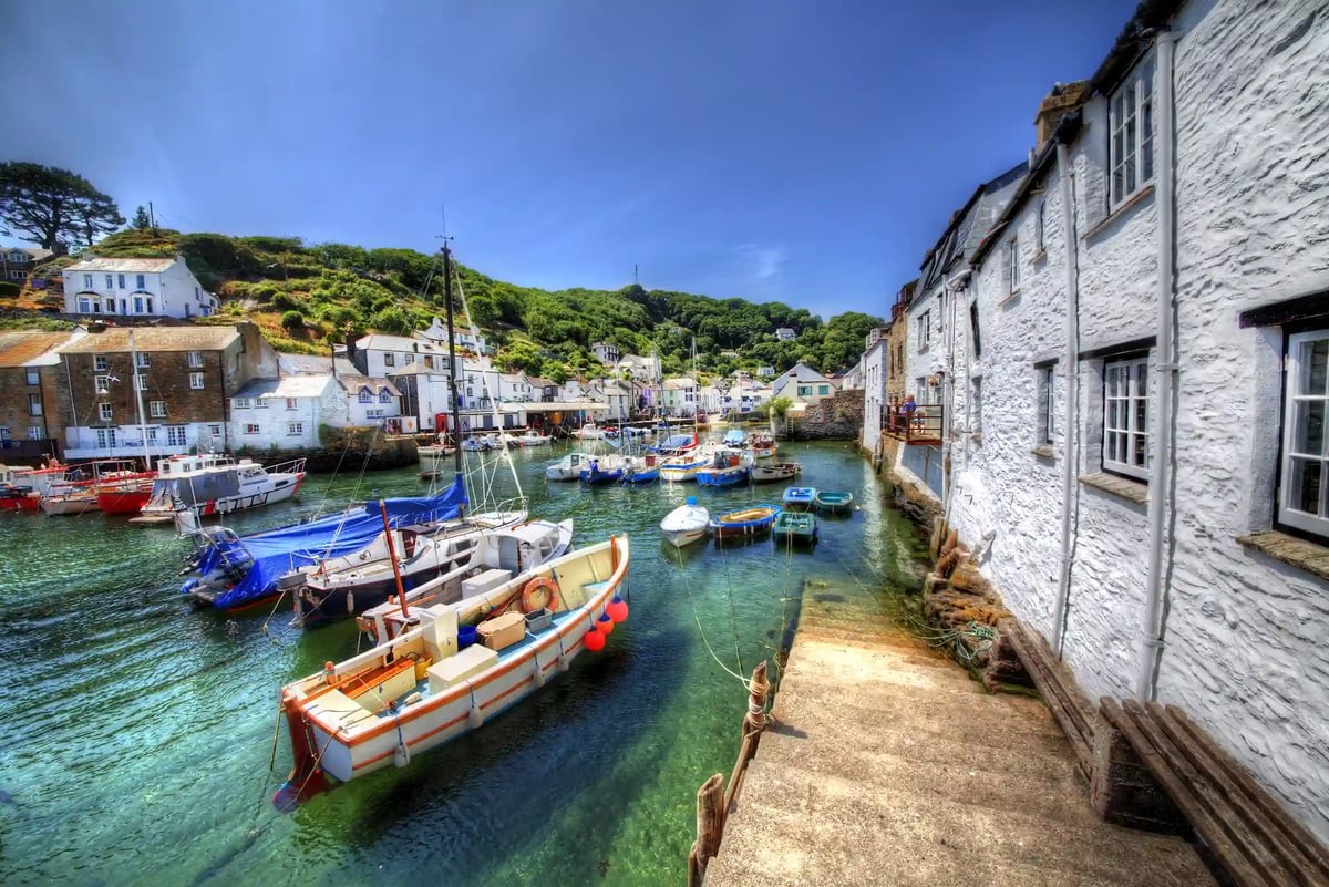 Kleiner Hafen in Polperro mit bunten Booten im klaren Wasser, weissen Häusern und grünen Hügeln im Hintergrund