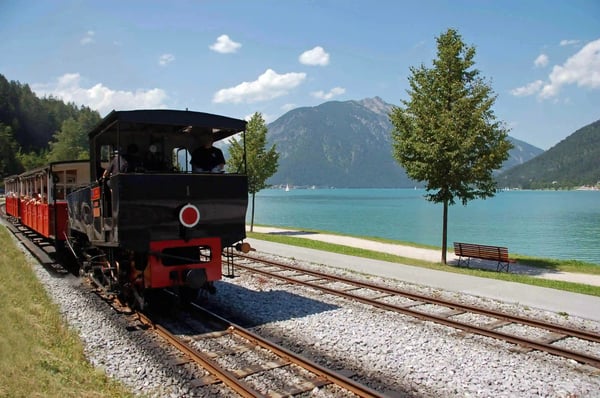 Historische Dampflok mit Reisenden und Musikanten auf einer Bahnstrecke in den Alpen