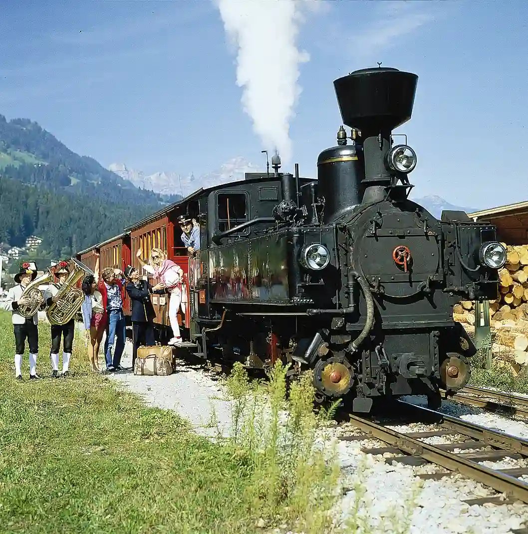 Historische Dampflok mit Reisenden und Musikanten auf einer Bahnstrecke in den Alpen