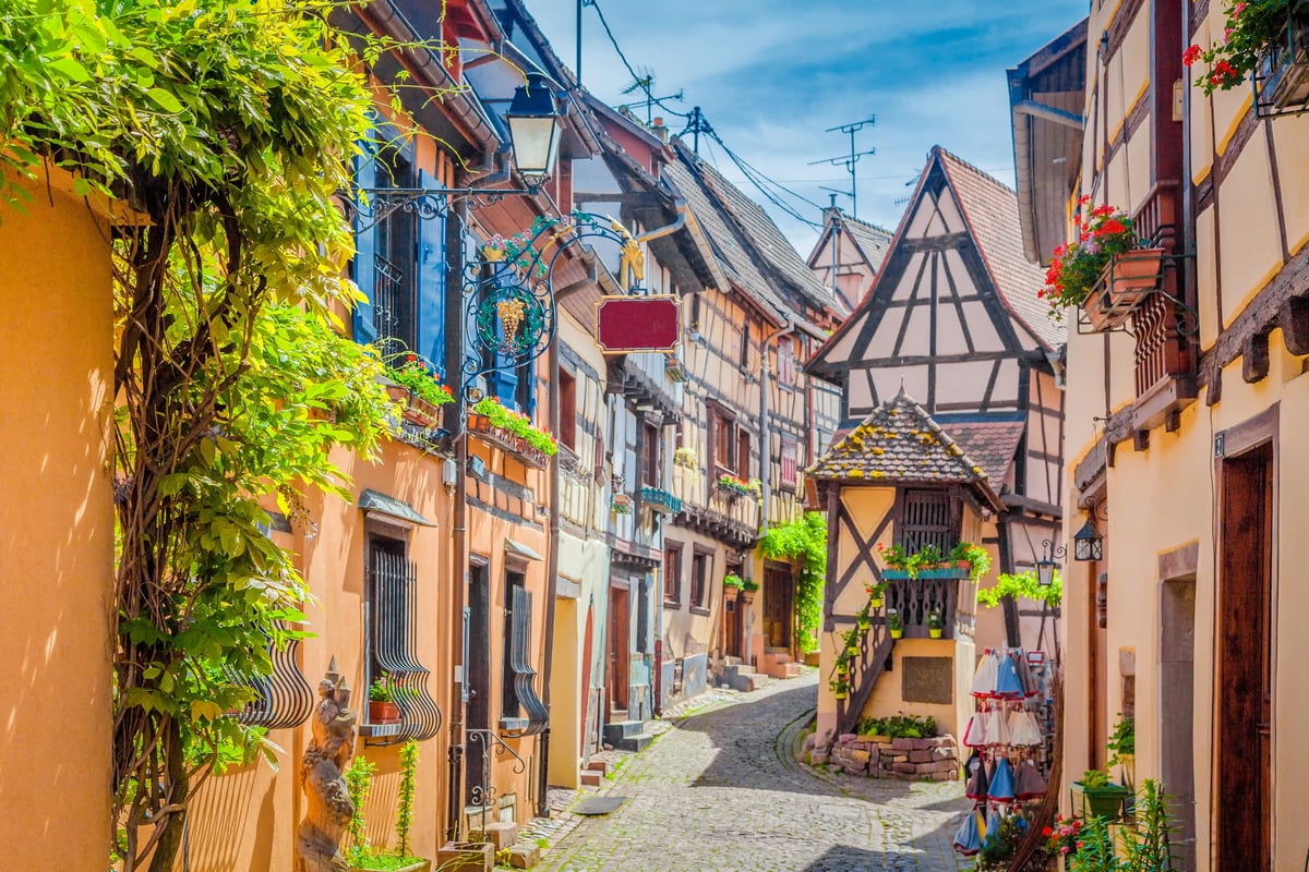 Malerische Gasse mit bunten Fachwerkhäusern, Blumenkästen an Fenstern und Kopfsteinpflaster in einem historischen Dorf im Elsass