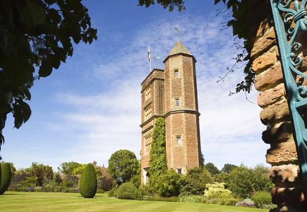 Backsteinturm mit Fahne in Schlossgarten, gruene Rasenfläche und Blumenrabatten unter blauem Himmel