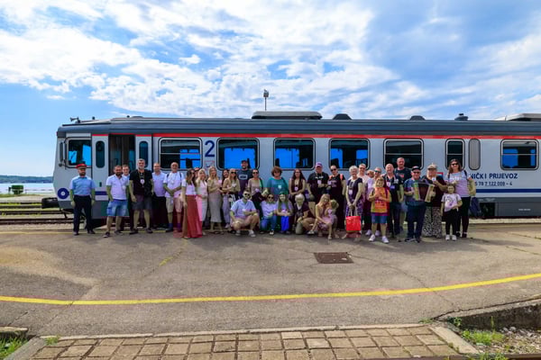 Gruppe von Reisenden steht auf einem Bahnsteig vor einem silbernen Zug unter blauem Himmel