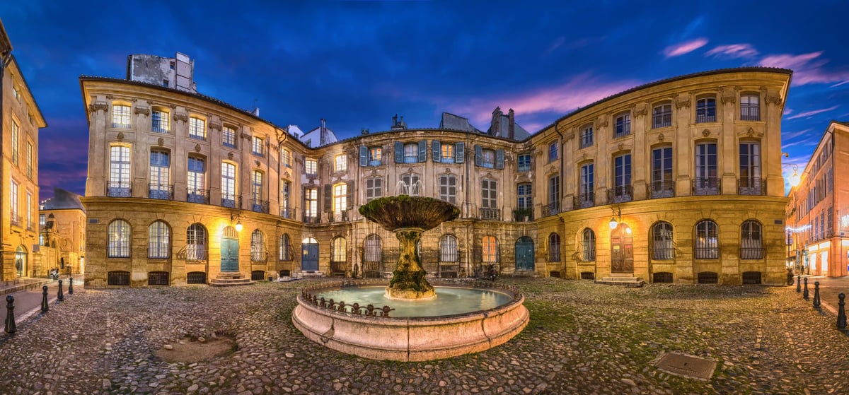 Place historique à Aix en Provence avec fontaine centrale, façades éclairées et ciel du soir aux couleurs chaudes