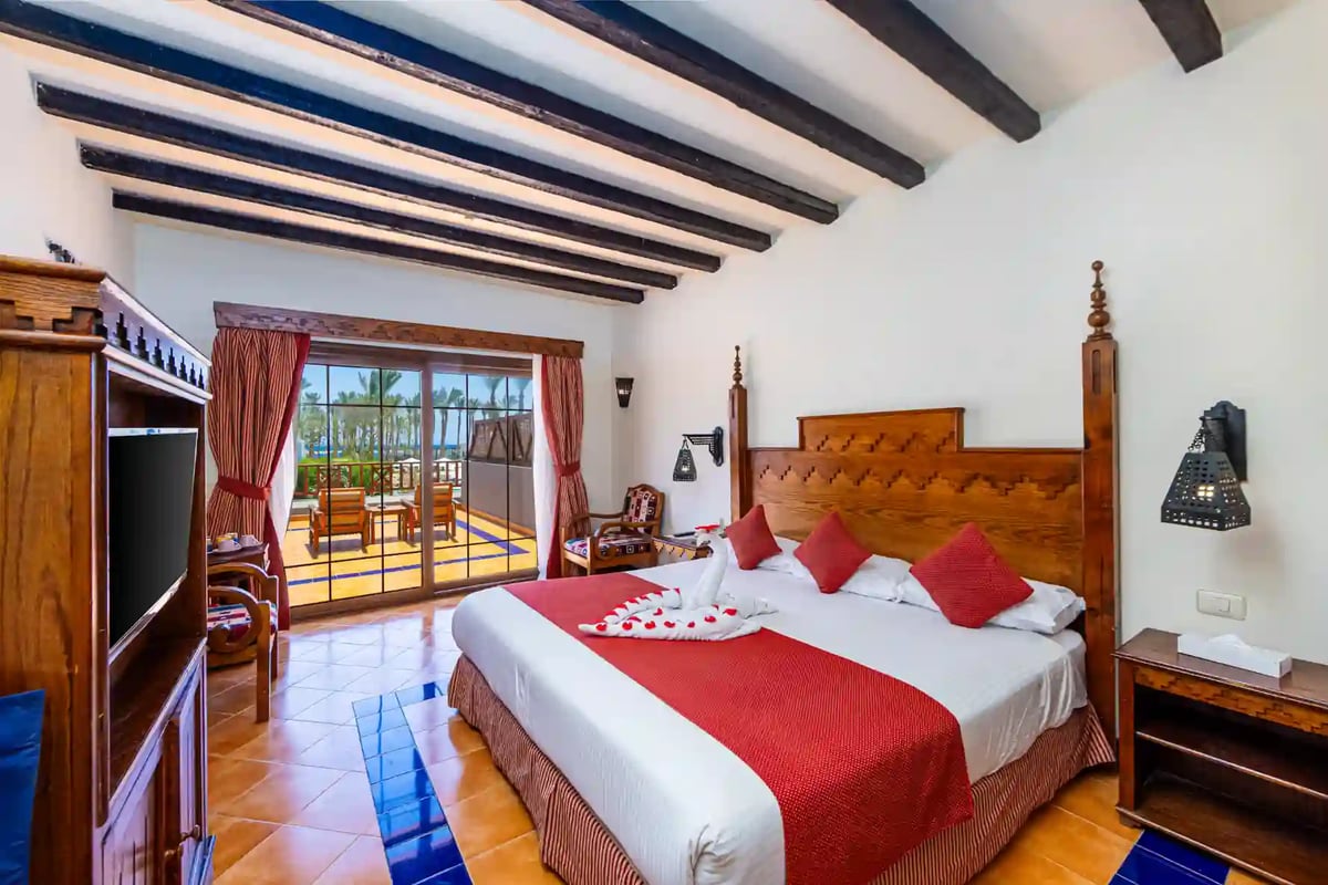 Grosszügiges Hotelzimmer mit Doppelbett, Holzdecke, Balkon und Blick auf Palmen in ägyptischem Strandresort