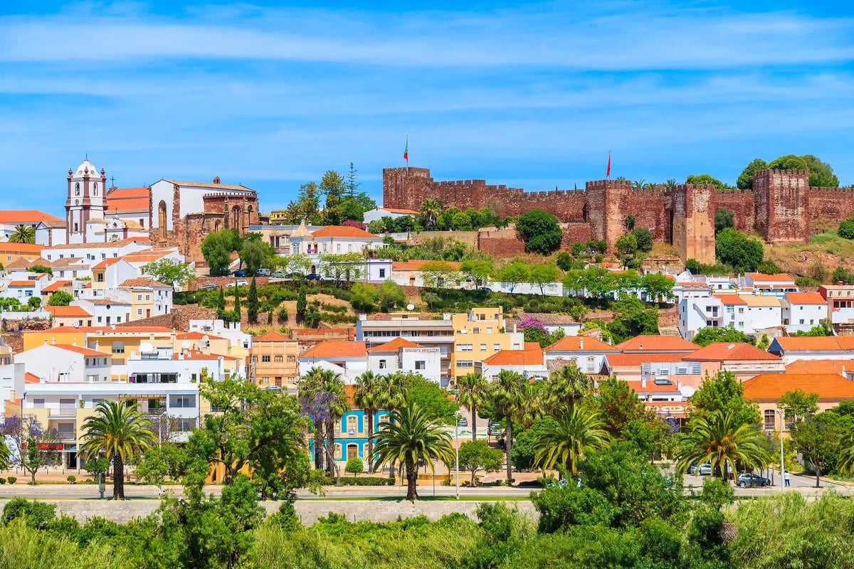 Historische Stadt Silves mit maurischer Burg, Kirche und farbigen Häusern zwischen Palmen unter blauem Himmel