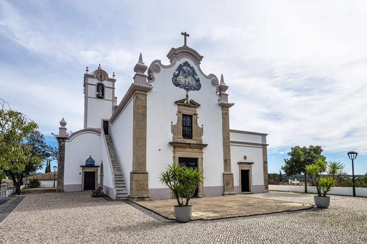Weisse barocke Kirche São Lourenço mit Glockenturm und dekorativer Fassade auf gepflastertem Platz in der Algarve