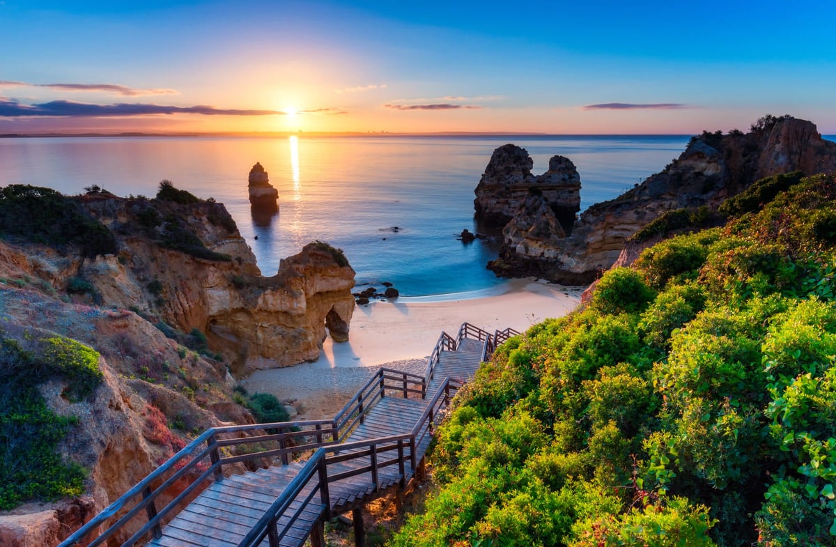 Malerische Bucht bei Lagos mit Felsen, Holztreppe und Sonnenuntergang über dem Meer