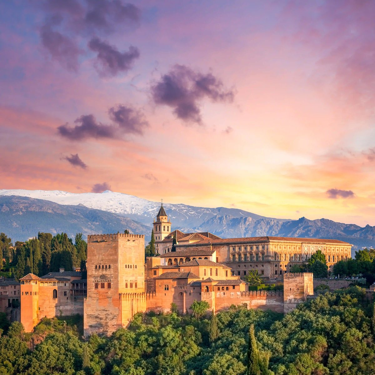 Die Alhambra in Granada mit Türmen und Mauern vor Bergen im warmen Abendlicht