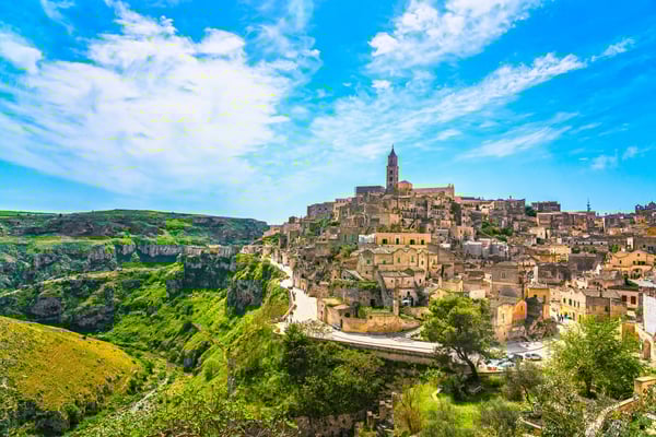 Weitblick auf die historische Altstadt von Matera mit steinernen Häusern, Kirche auf dem Hügel und grüner Schlucht im Vordergrund