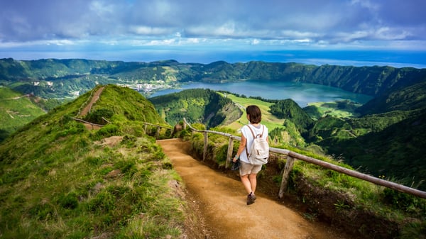 Wanderin auf schmalem Pfad mit Blick auf grüne Berge und einen Kratersee