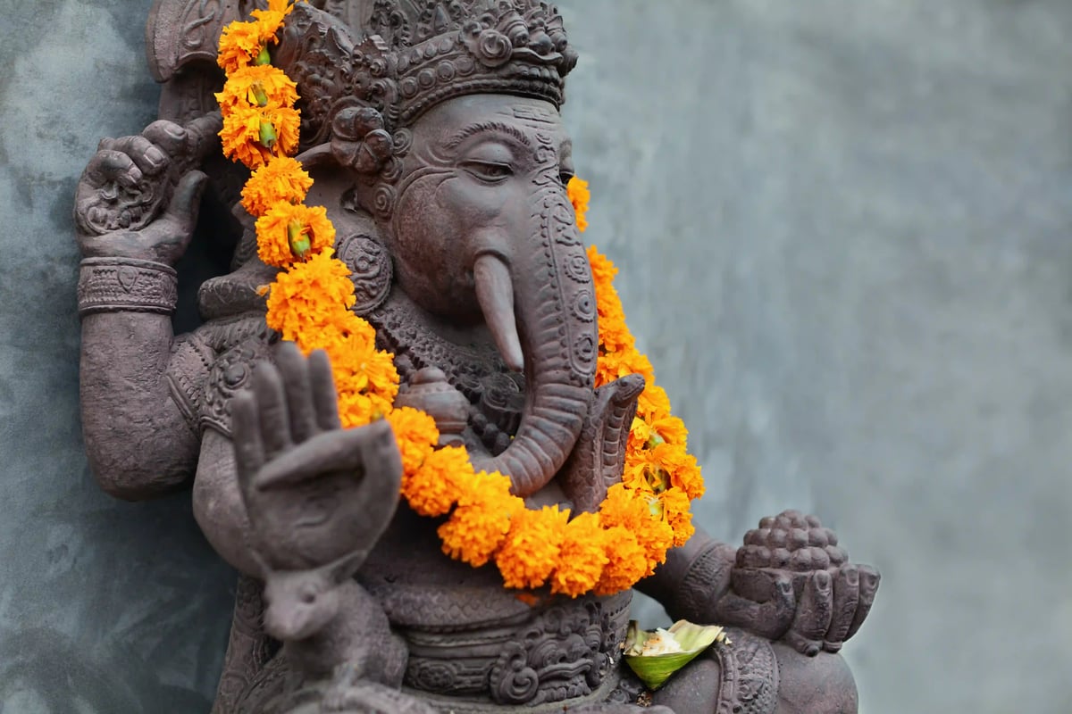 Steinerne Ganesha Statue mit Blumenkranz und erhobener Hand vor neutralem Hintergrund