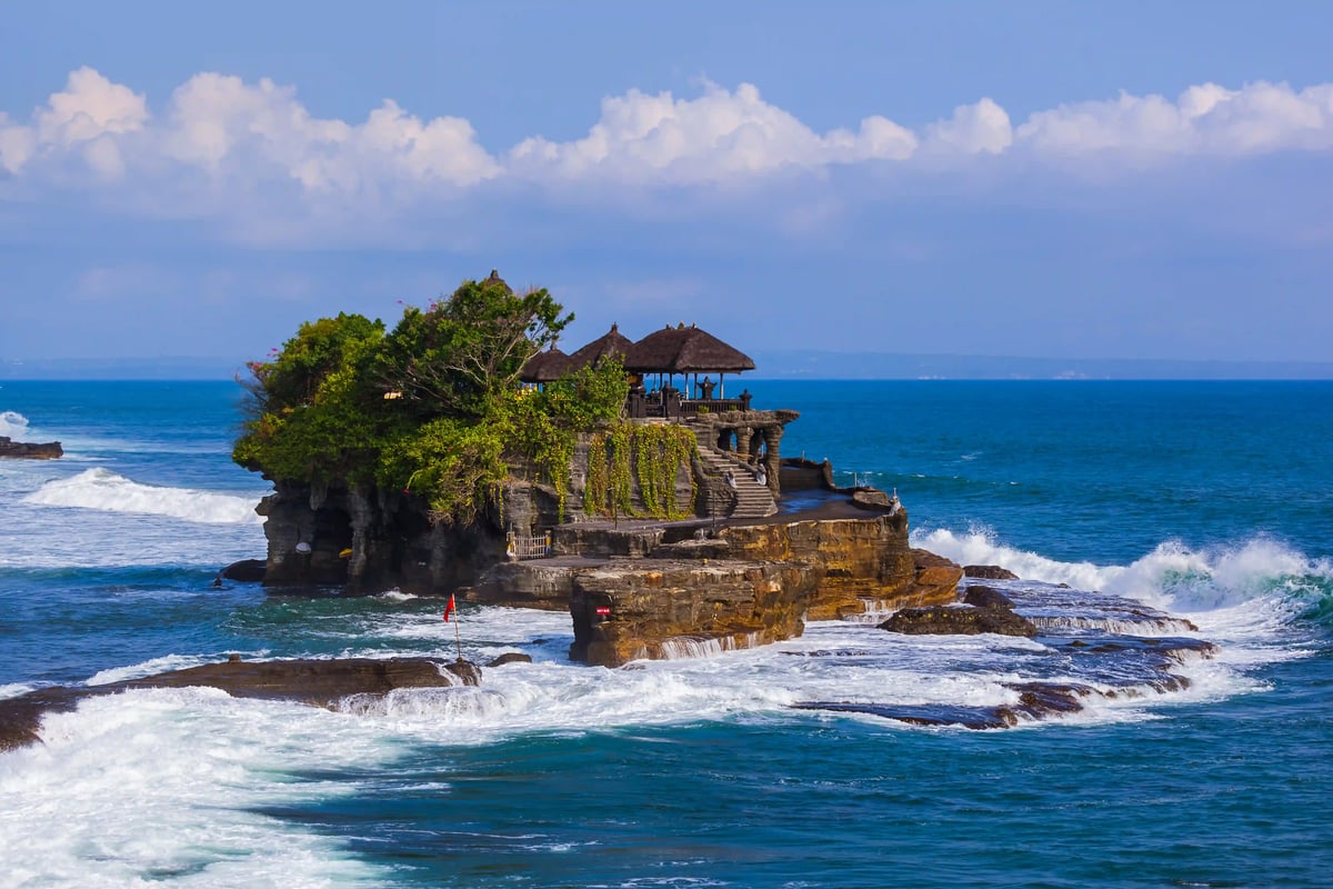 Tanah Lot Tempel auf einem Felsen im Meer mit Wellen und blauem Himmel