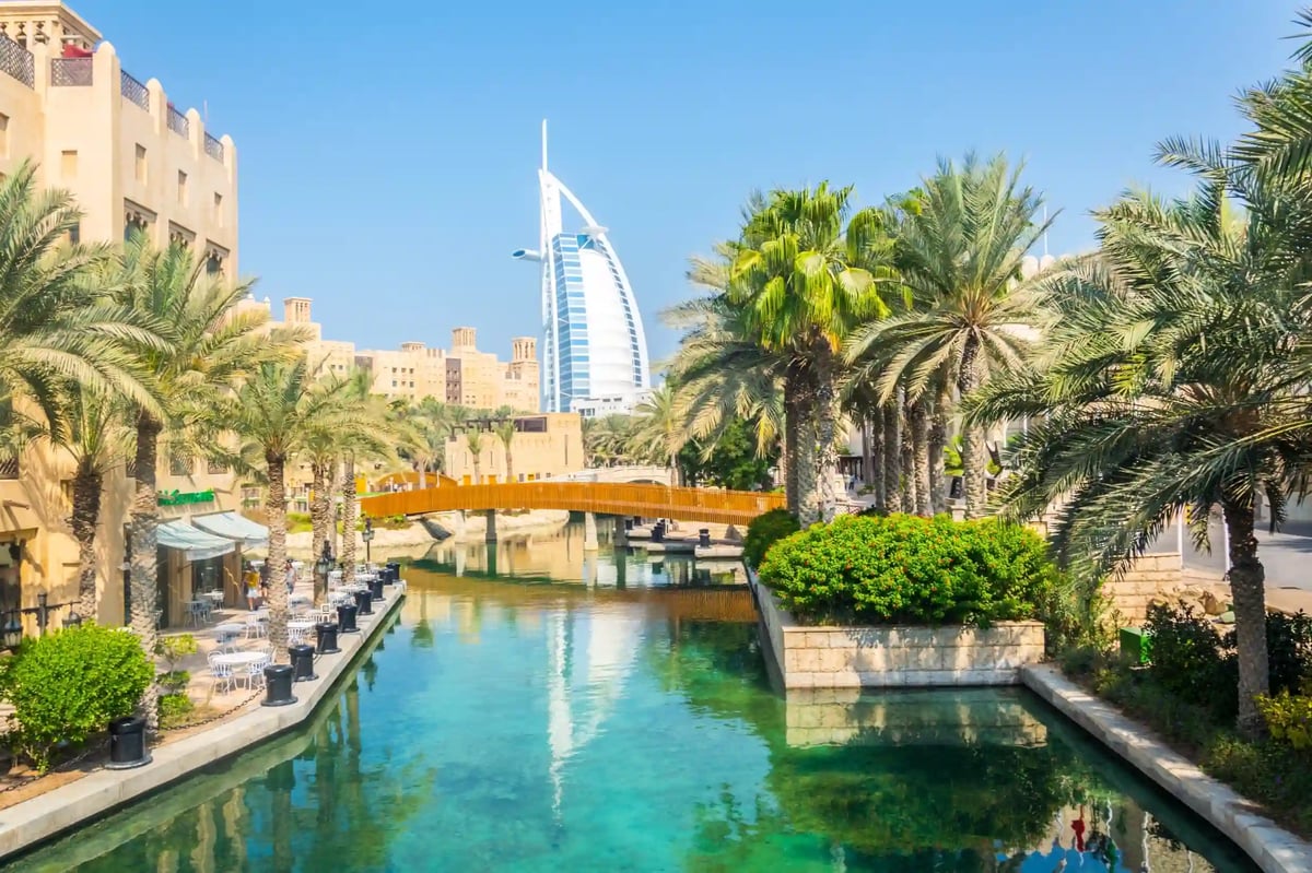 Blick über Wasserkanal und Palmen auf den Burj al Arab bei Tageslicht