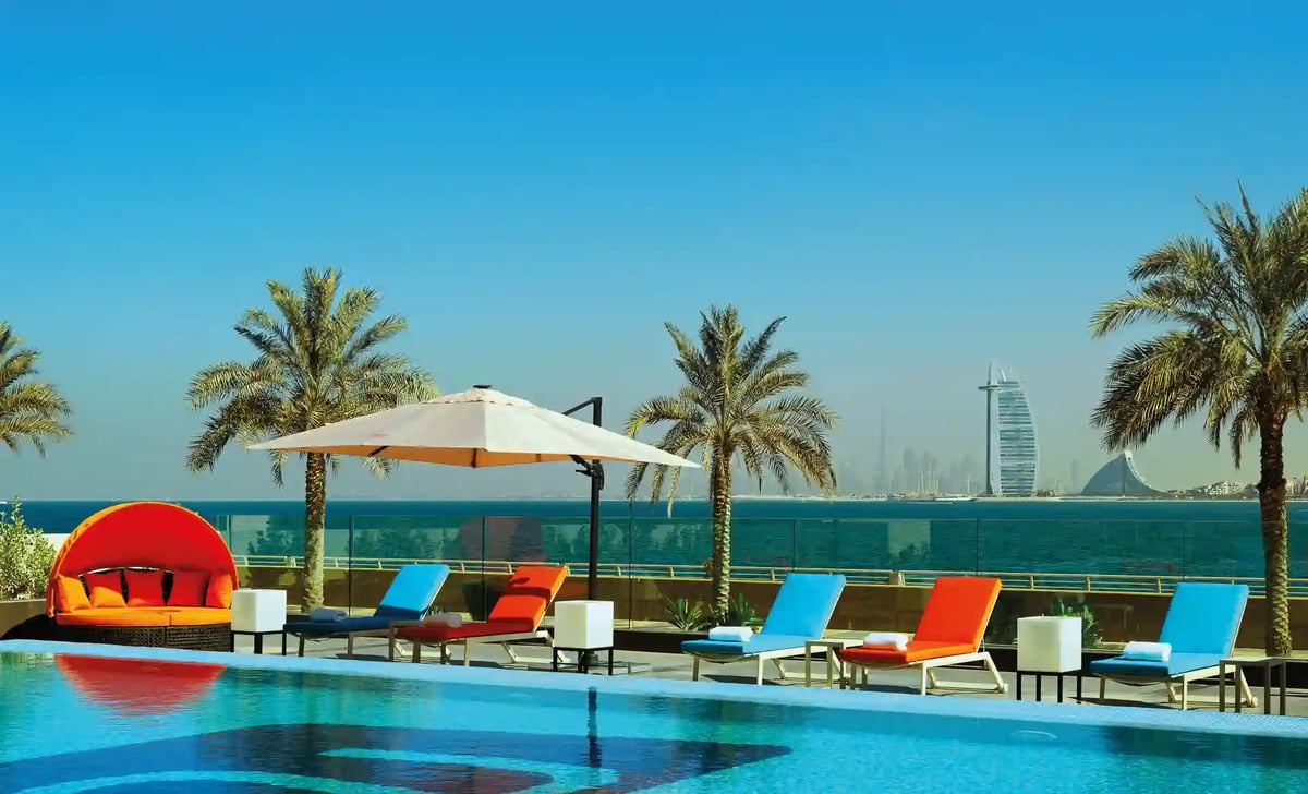 Hotelpool mit Sonnenliegen und Palmen mit Blick auf das Meer und die Skyline von Dubai