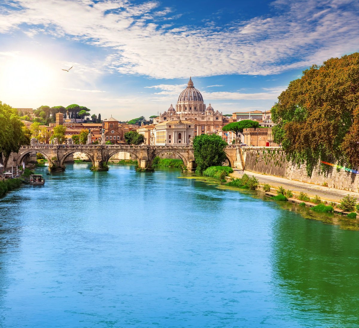Blick über den Fluss Tiber auf eine Brücke und den Petersdom im Hintergrund