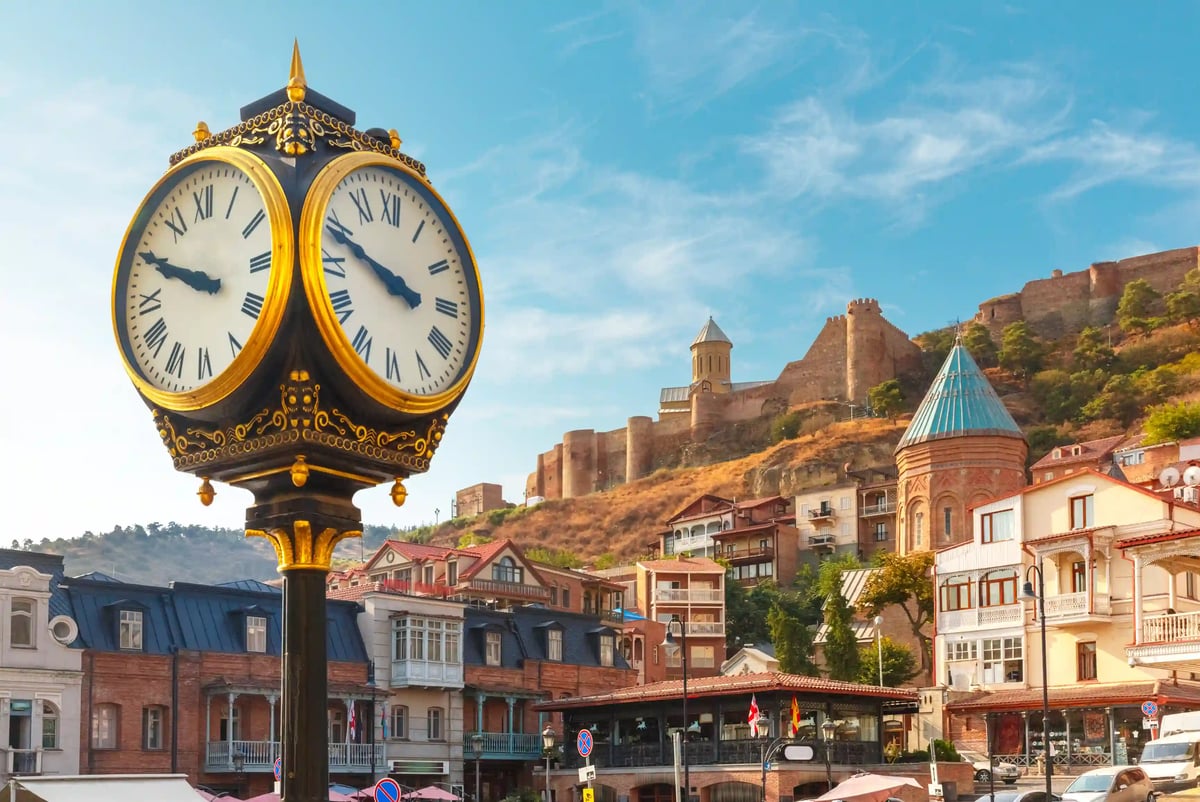 Historische Uhr im Vordergrund mit Blick auf die Altstadt von Tiflis und eine Festung auf dem Hügel