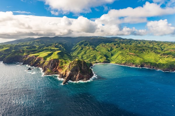 Küste von Maui mit steilen Klippen, grüner Vegetation und blauem Meer aus der Luft gesehen