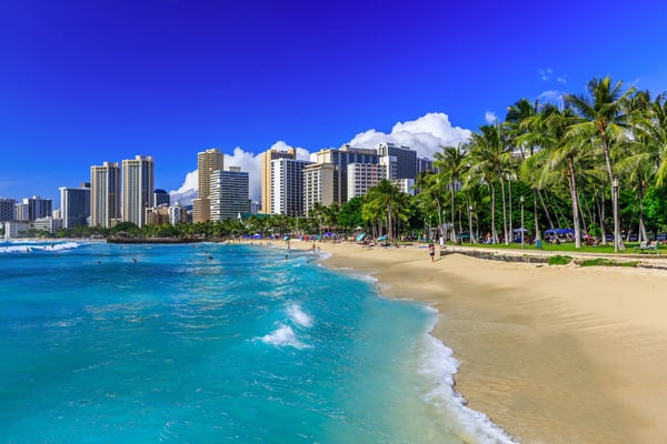 Waikiki Beach auf Oahu mit Sandstrand, Palmen, Badenden und Hochhäusern entlang der Küste