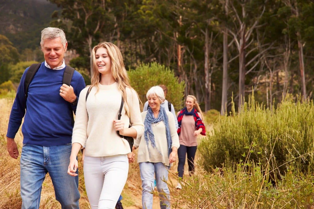 Mehrgenerationengruppe wandert gemeinsam auf einem Naturweg durch lichte Waldlandschaft