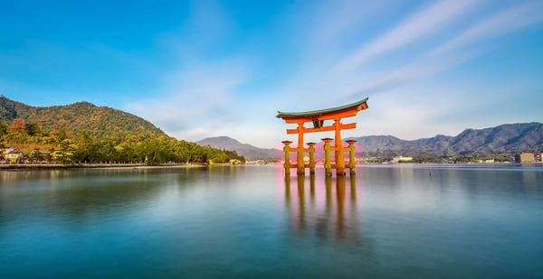 Rotes Torii-Tor des Itsukushima Schreins im Wasser vor bewaldeten Bergen