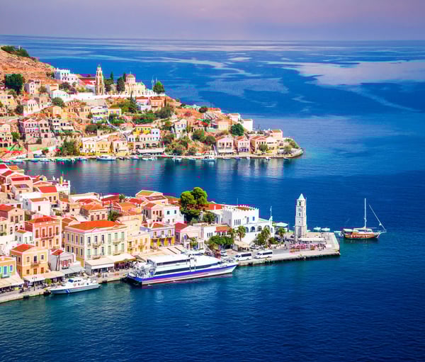 Panoramablick auf den hufeisenförmigen Hafen von Symi mit dicht bebauten Hängen und ruhigem Mittelmeer