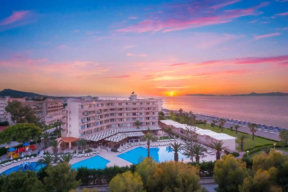 Hotelanlage am Meer bei Sonnenuntergang mit Poollandschaft, Palmen und ruhiger Strandlinie