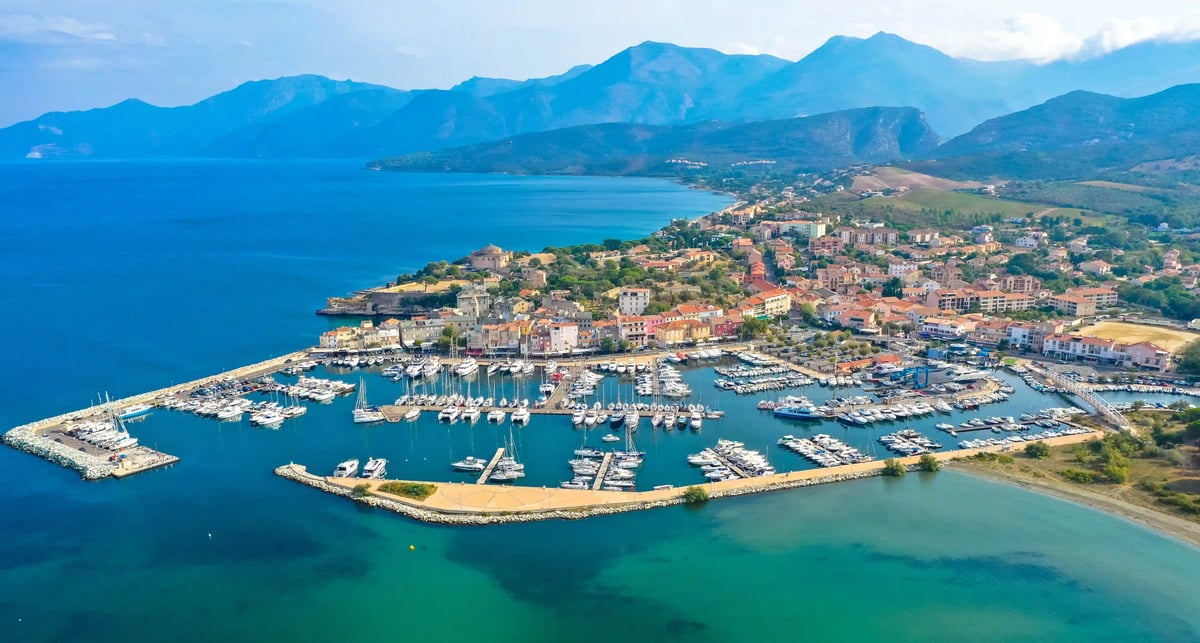 Luftaufnahme des Hafens von Calvi mit Segelbooten, Altstadt und Berglandschaft entlang der Küste