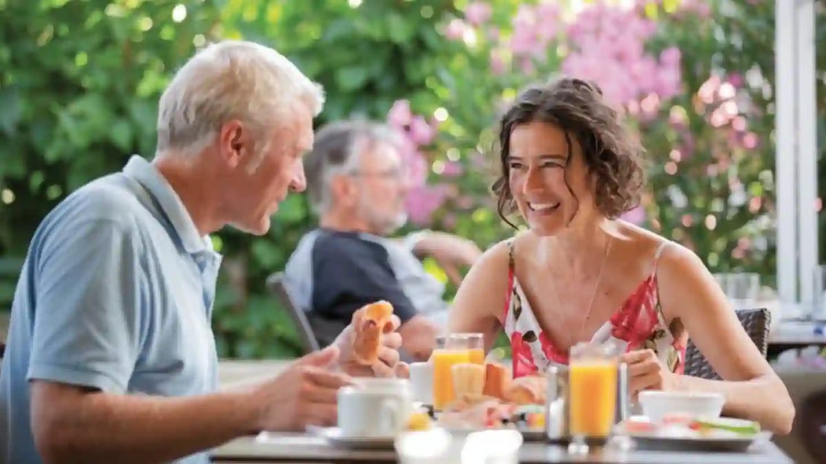 Mann und Frau sitzen beim Frühstück im Garten und unterhalten sich an einem Tisch mit Saft und Gebäck
