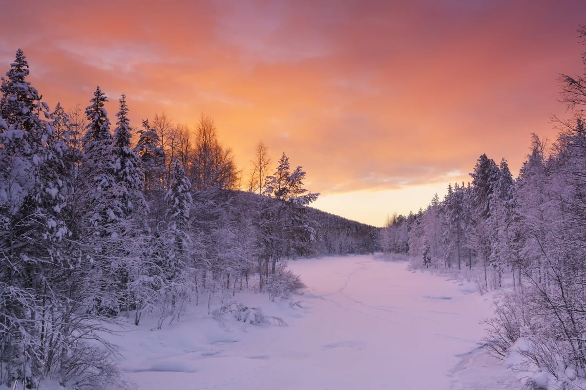 Verschneiter Flusslauf in nordischer Winterlandschaft bei Sonnenuntergang