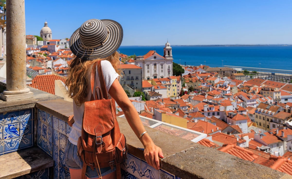 Femme avec chapeau regardant les toits de Lisbonne et l’océan Atlantique