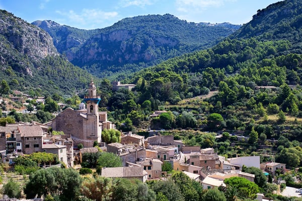 Traditionelles Bergdorf Valldemossa mit Steinhäusern und Kirche eingebettet in grüne Hügel auf Mallorca