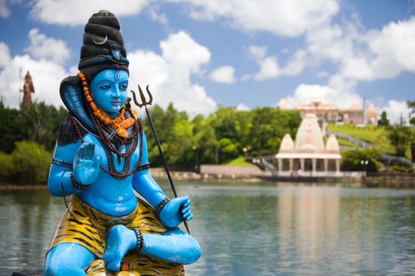 Blaue Shiva-Statue am See Grand Bassin mit Tempelanlage im Hintergrund