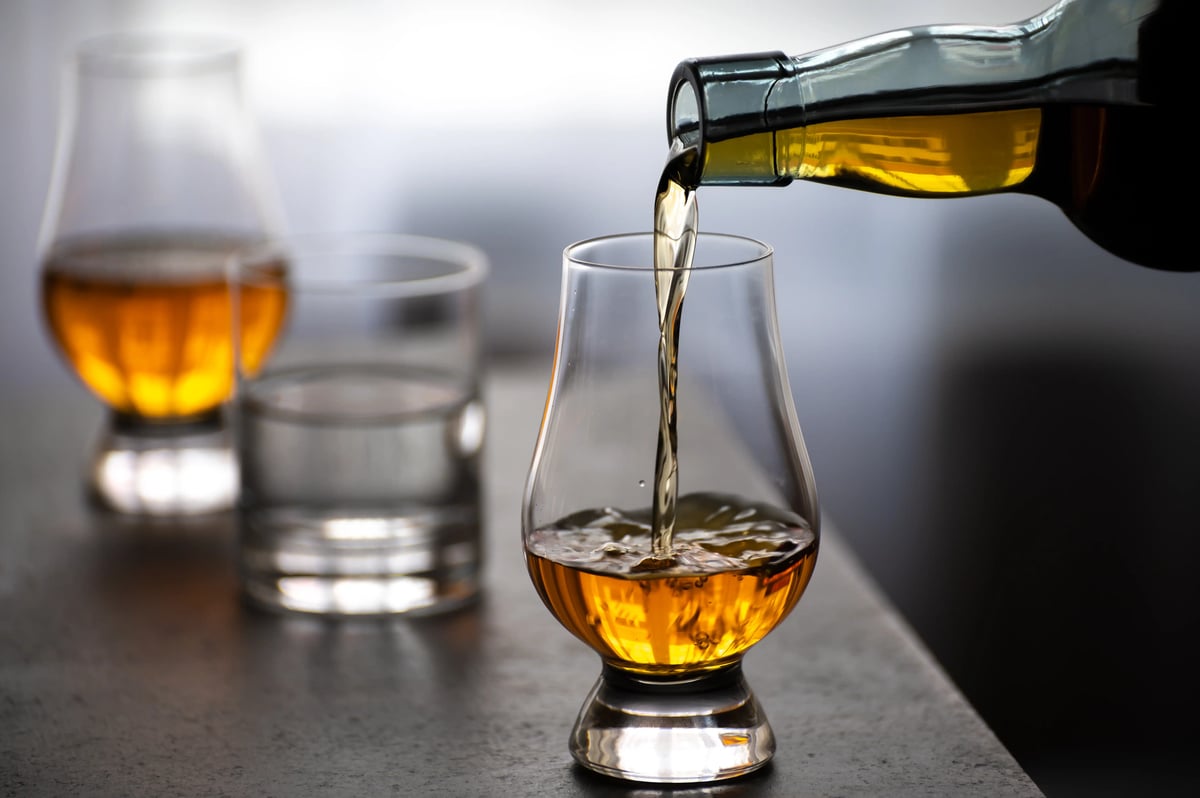 Whisky wird in ein Glas eingeschenkt, daneben stehen weitere Gläser