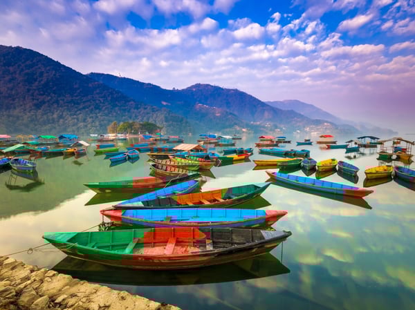 Viele bunte Boote auf dem ruhigen Phewa See mit Bergen im Hintergrund