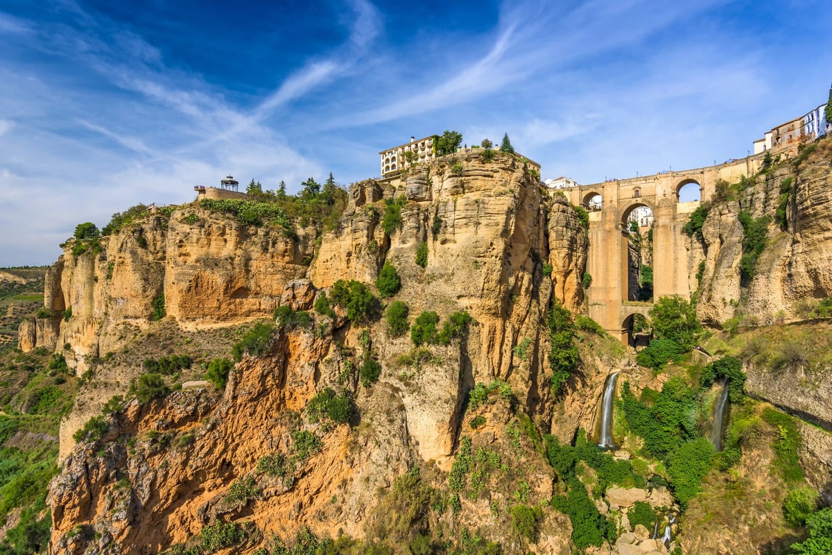 Tiefe Schlucht von Ronda mit steilen Felswänden, historischer Brücke und grünem Bewuchs unter blauem Himmel