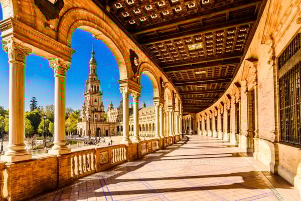 Arkadengang der Plaza de España in Sevilla mit hohen Säulen, warmem Licht und Blick auf einen Turm