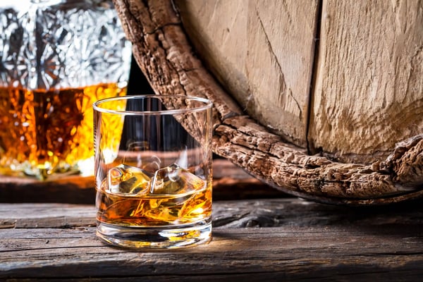 Glas mit Whisky vor Holzfass