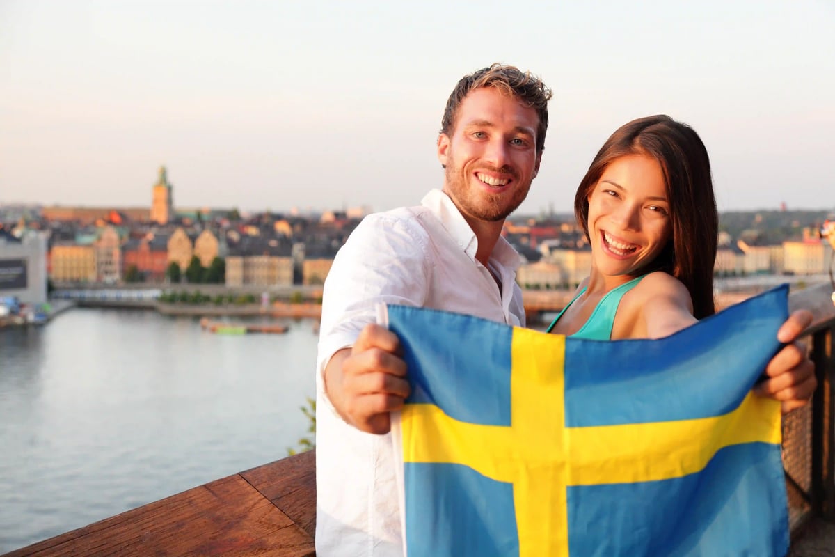 Fröhliches Paar hält schwedische Flagge mit Blick auf Stockholm bei Sonnenuntergang