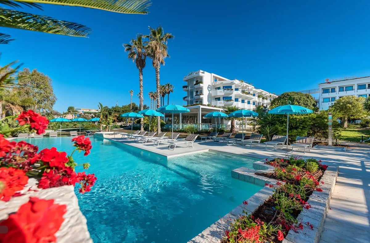 Moderne Hotelanlage mit grossem Swimmingpool, Palmen, Sonnenschirmen und Liegestühlen in ruhiger Urlaubsatmosphäre