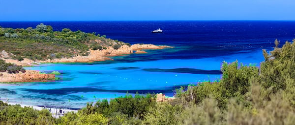 Kleine Badebucht mit hellem Sand, klarem Wasser und Felsen an der Costa Smeralda