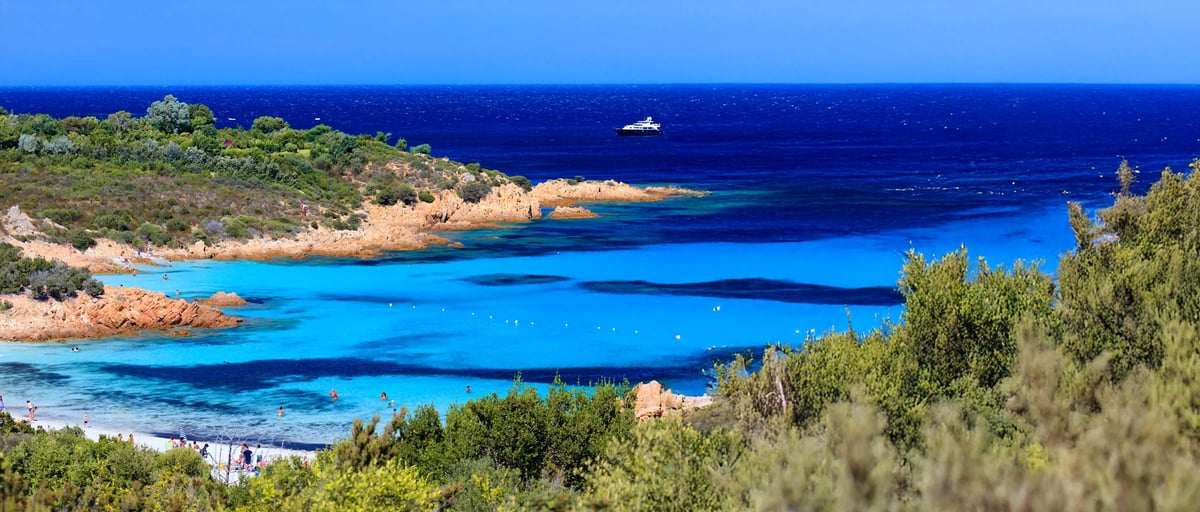 Kleine Badebucht mit hellem Sand, klarem Wasser und Felsen an der Costa Smeralda