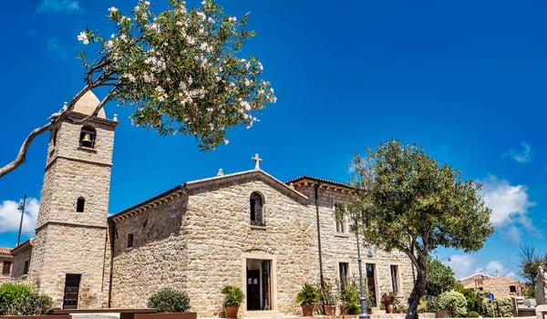Historische Steinkirche mit Glockenturm und Olivenbaum unter blauem Himmel