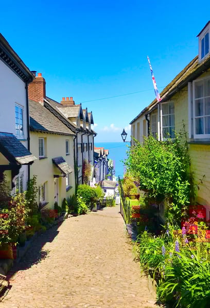 Steile Kopfsteinpflastergasse in Clovelly mit historischen Häusern, Blumen und Blick auf das Meer