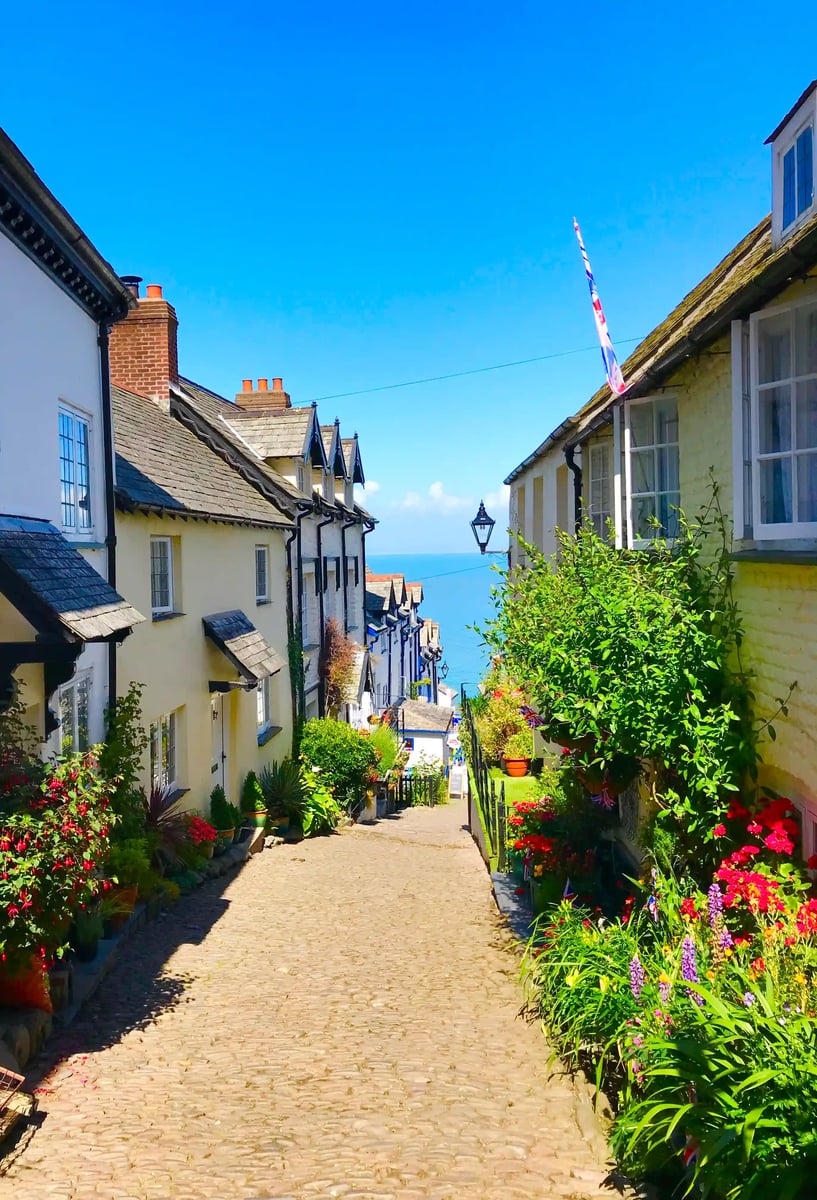 Steile Kopfsteinpflastergasse in Clovelly mit historischen Häusern, Blumen und Blick auf das Meer