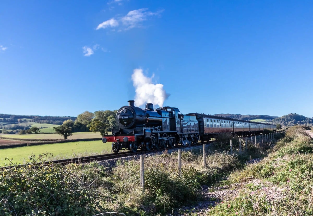 Schwarze Dampflokomotive der West Somerset Railway fährt durch ländliche Landschaft